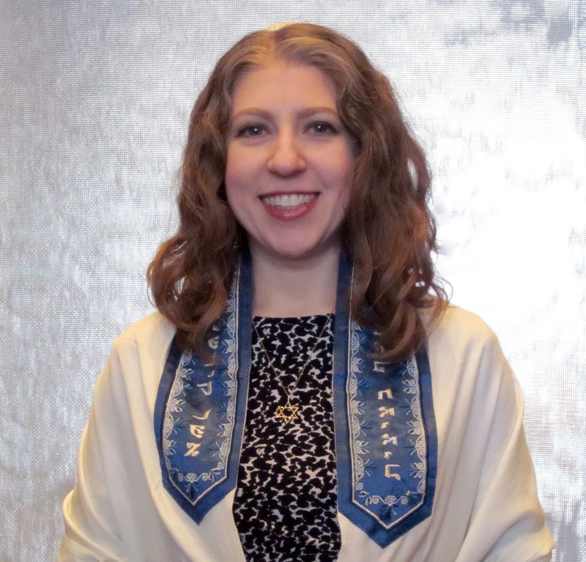 A photo of Cantor Lind smiling to the camera, wearing a tallit and a Star of David neckless